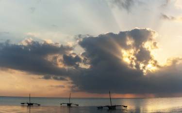 Sunrise behind the clouds with small fishing boats