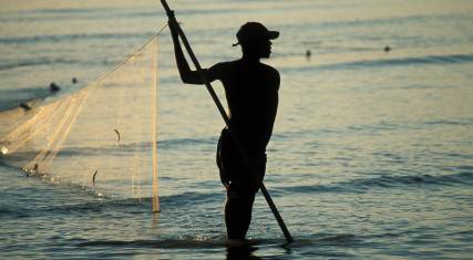 Fisher walking into the sea with a net at sunrise